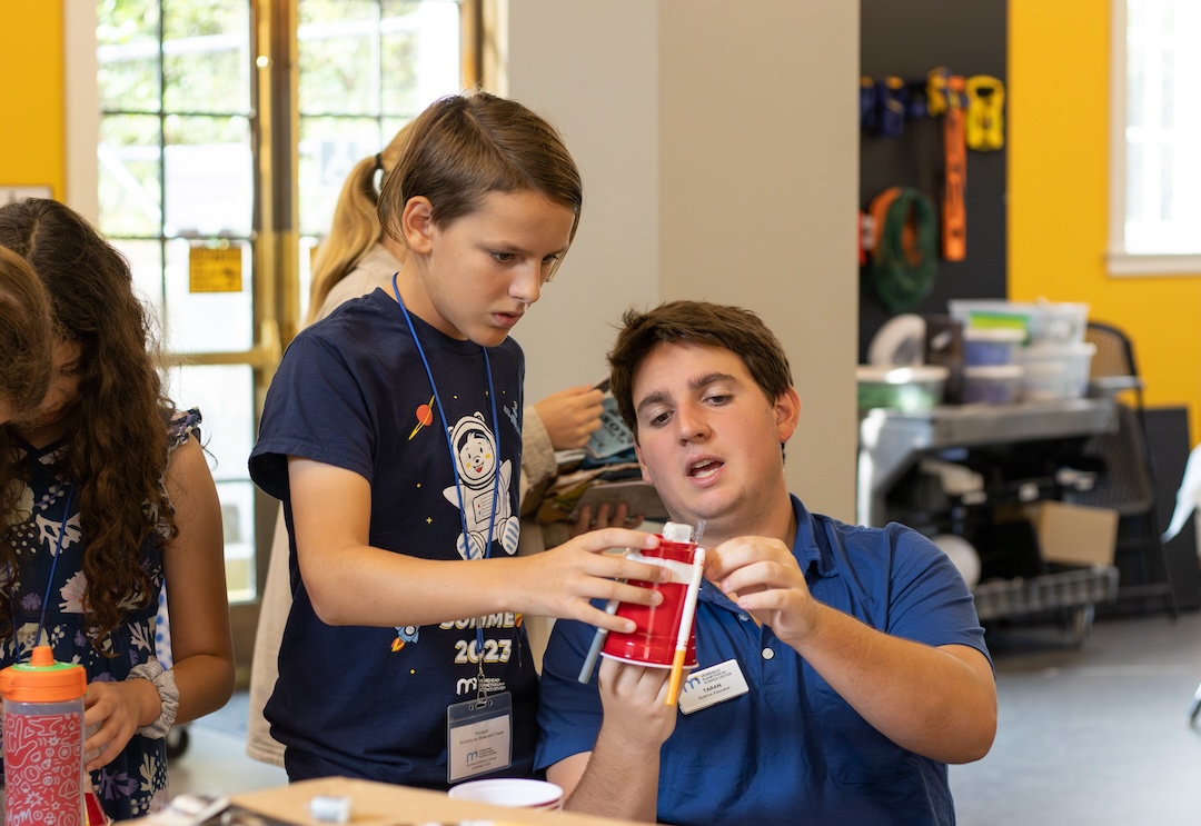 A Morehead employee helps a camper with a "wigglebot" made of a cup, markers, and a motor. 