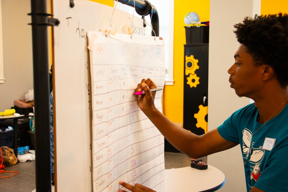 A person writes on paper attached to a board.