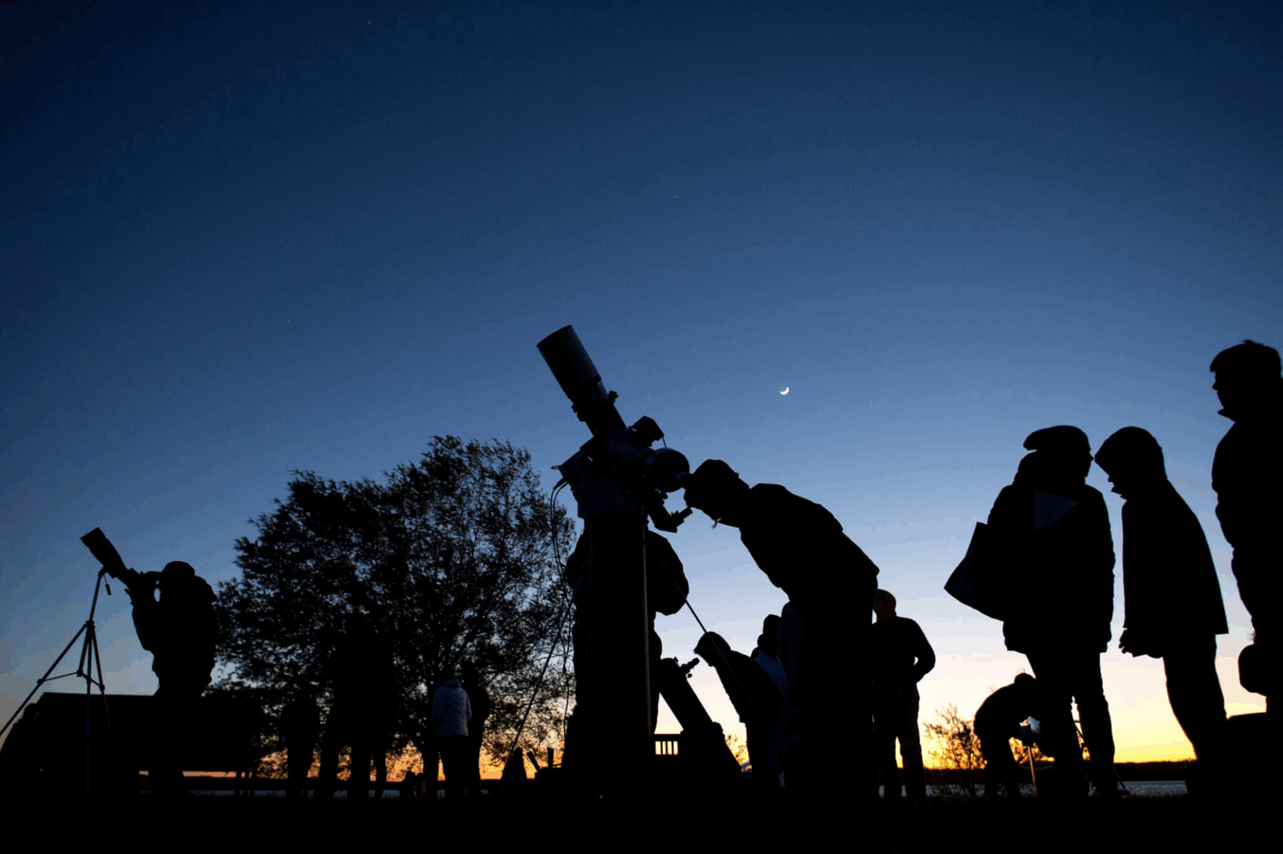 Silhouettes of people using telescopes at sunset.