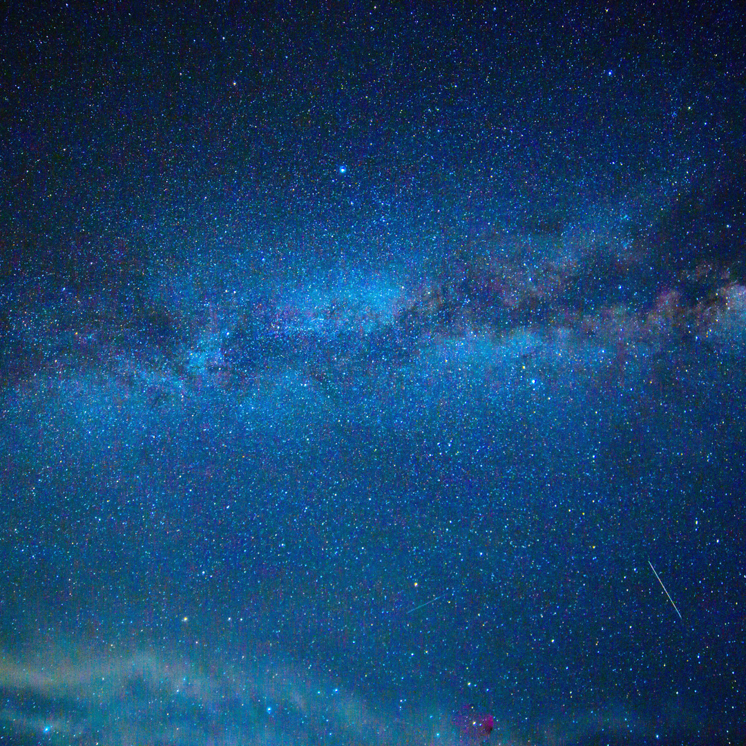 A field of stars with the trail of a meteor and nebulae.