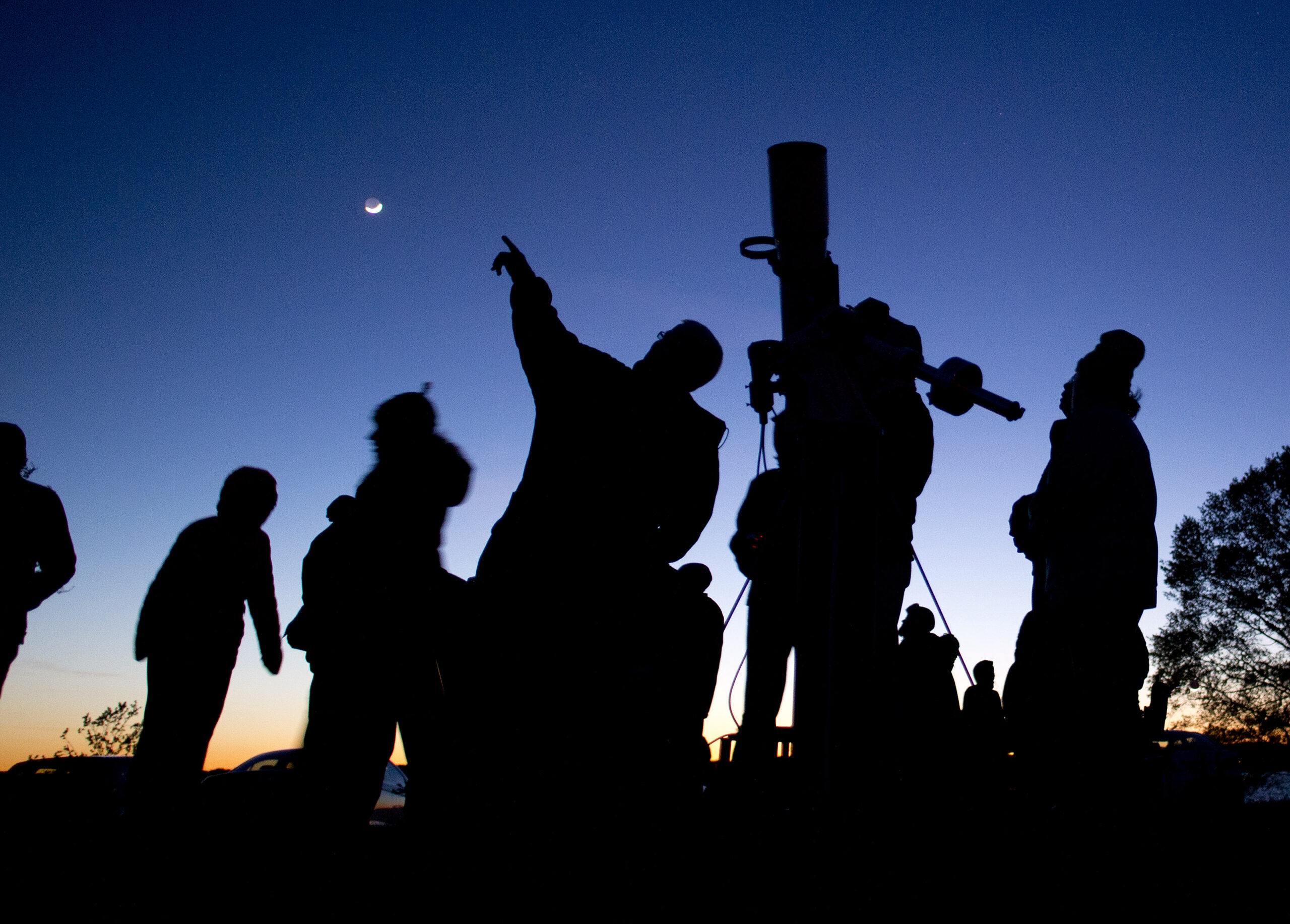 Silhouttes of people skywatching via telescope.