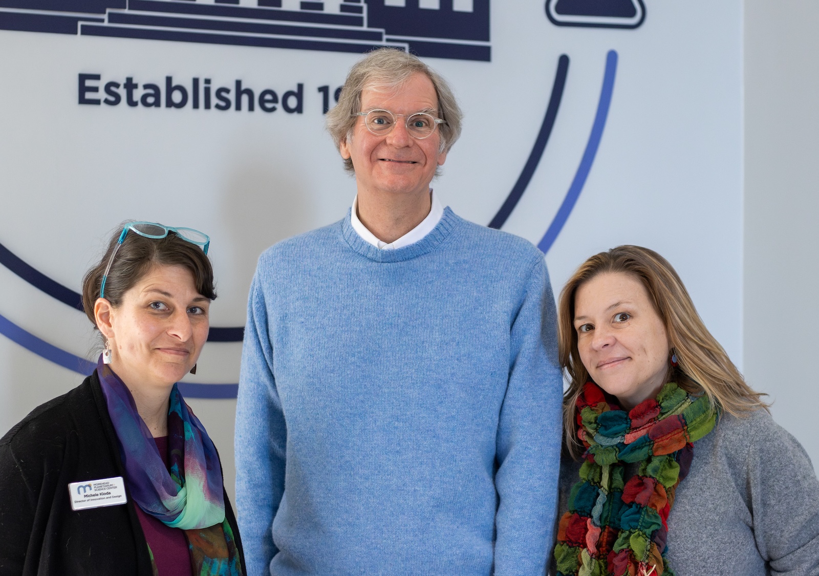 Three people stand against a wall.