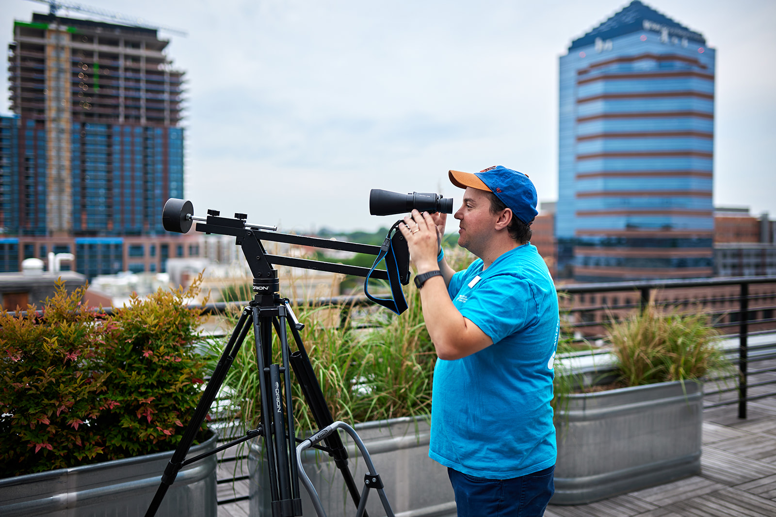 A Morehead employee looks through a pair of binoculars pointed at the sky. In the background is the Durham city skyline. 