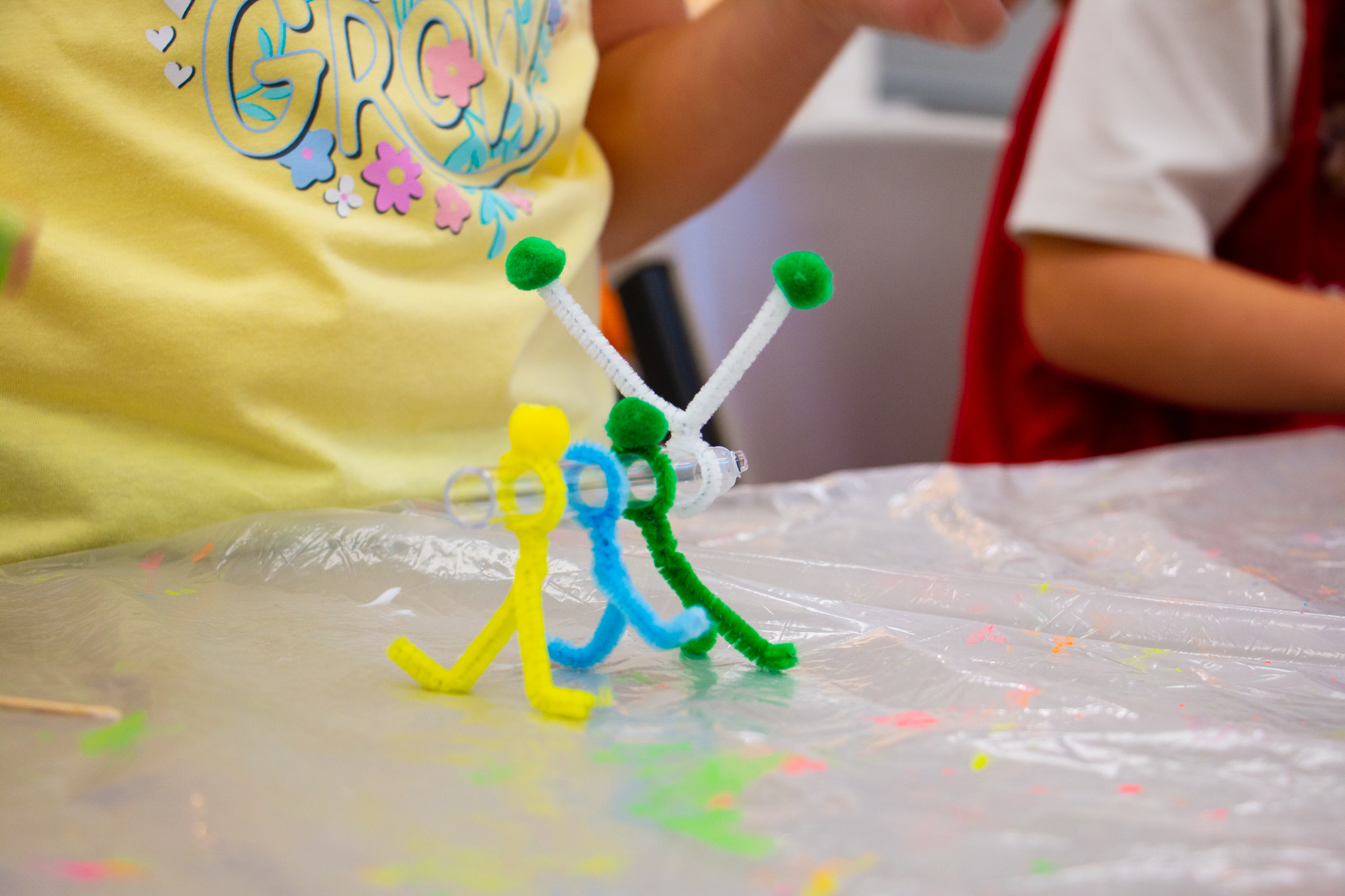 A caterpillar made out of pipe cleaners and clear lab tube. In the background are children. 