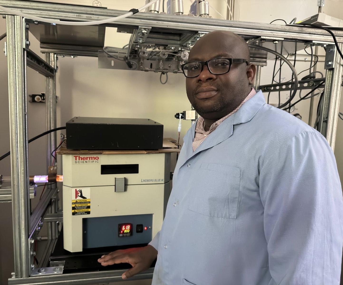 Oluwaseun Oyetade, a postdoctoral research associate, stands beside a plasma-enhanced chemical vapor deposition system (PECVD) for thin-film growth of carbon nanostructures, which have specific properties for use in various applications, such as electronics, photovoltaics and sensors.