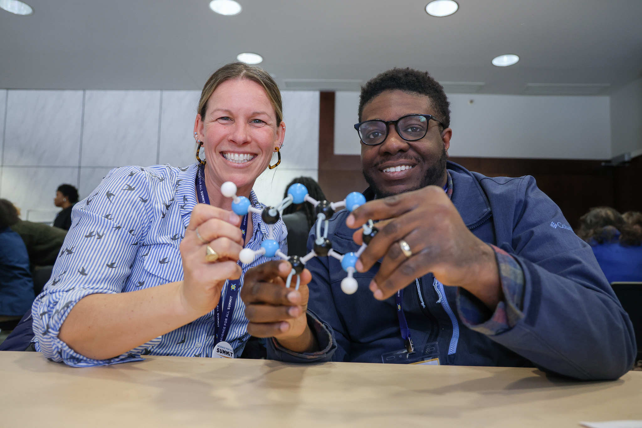 Two professionals smile while holding up a molecular model.