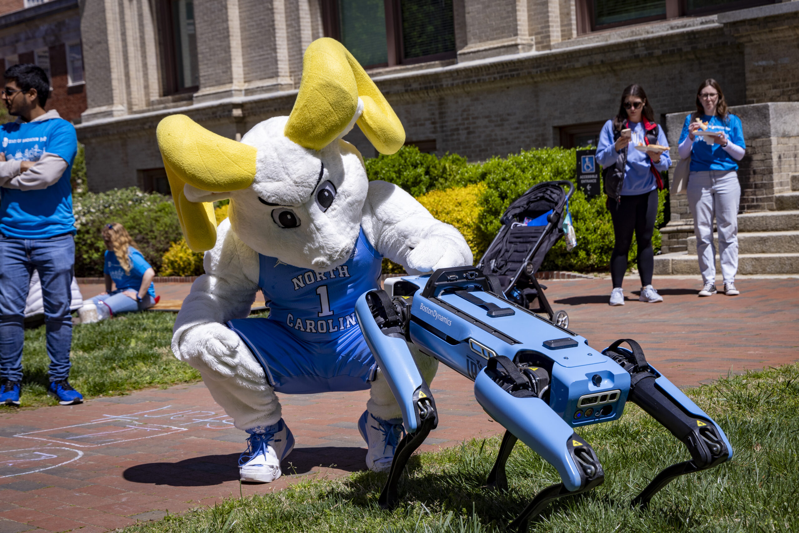Ramses, the UNC-Chapel Hill mascot, pets Spot, a Carolina blue robotic dog.