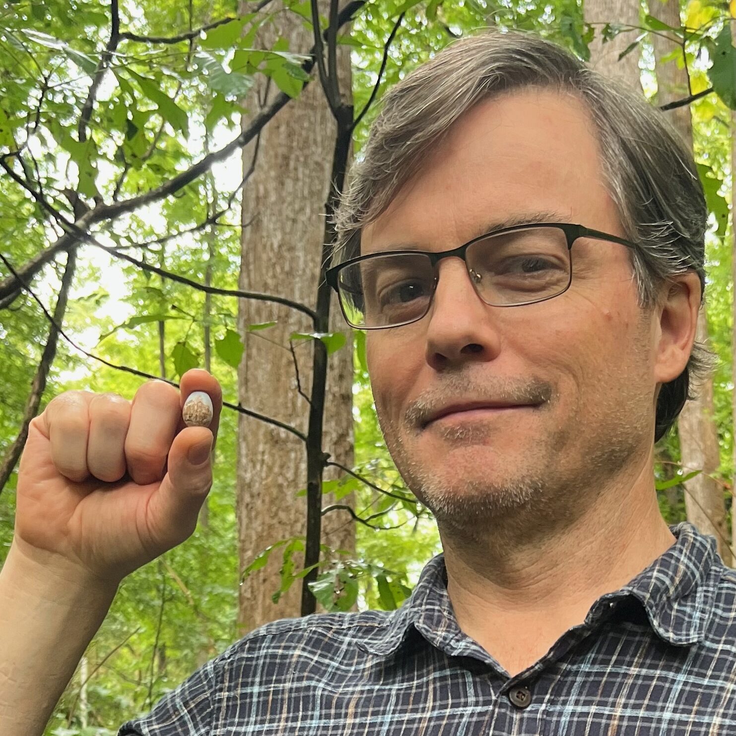 Dr. Keith Sockman holds up an acorn in a wooded area.