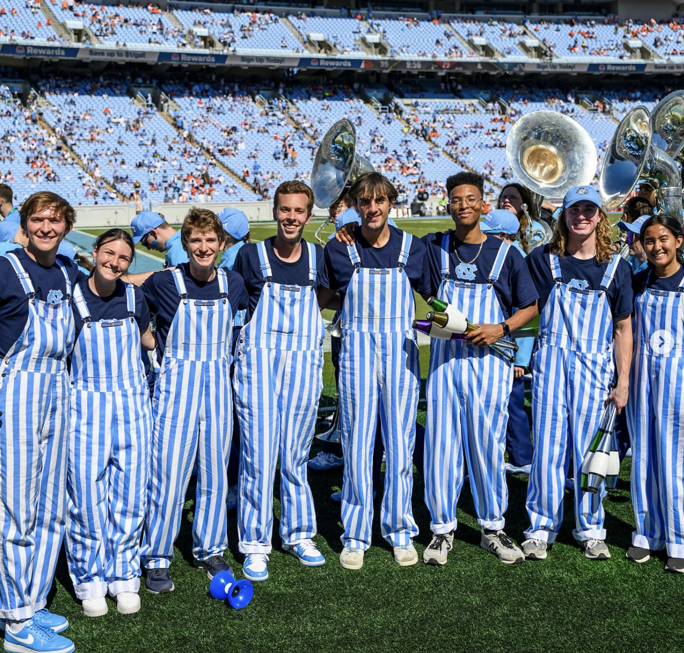The Juggling Club of Carolina stands on the field at Kenan Stadium, wearing white and Carolina Blue striped overalls.