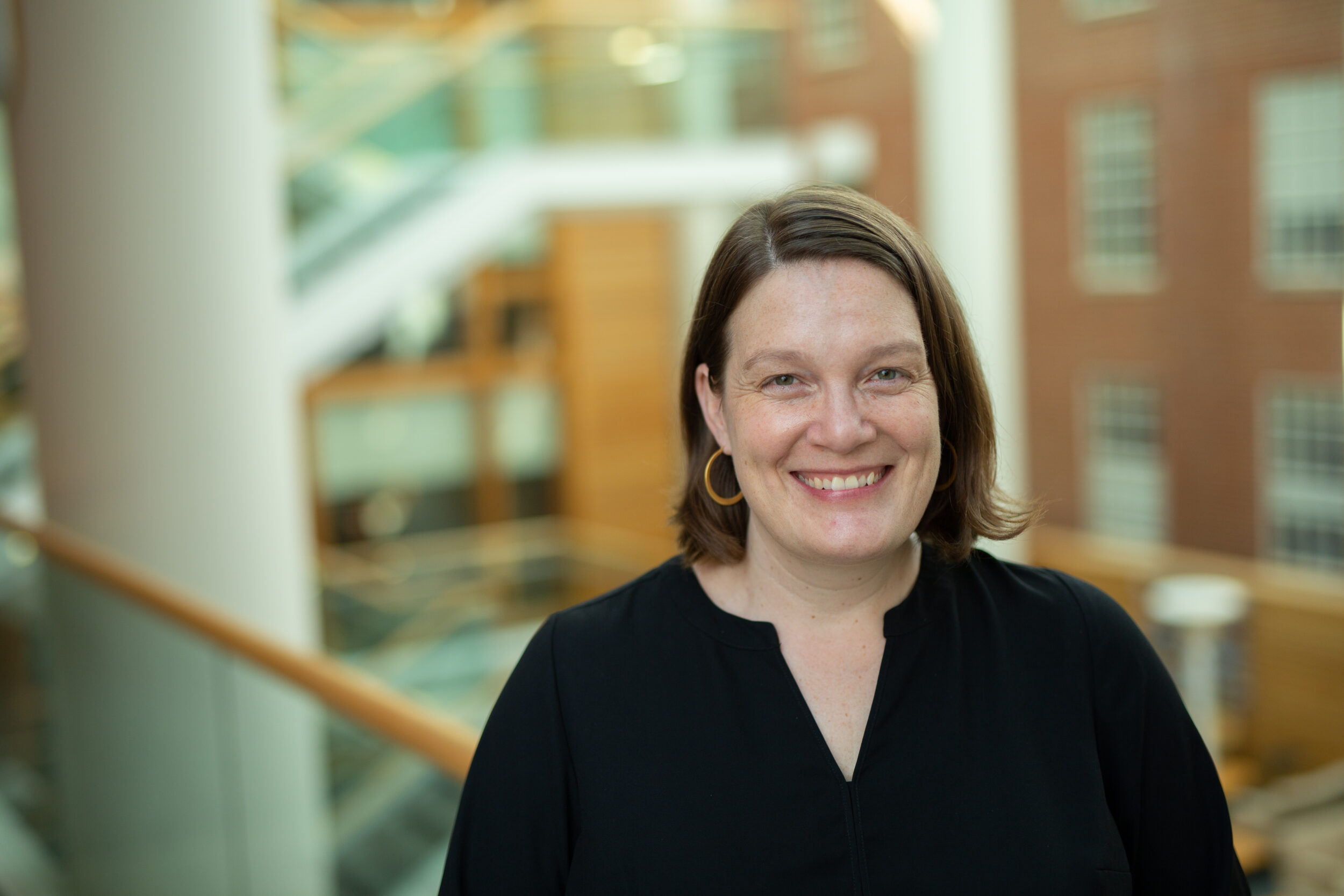 Dr. Melissa B. Gilkey smiles in a black blouse with campus buildings in the background.