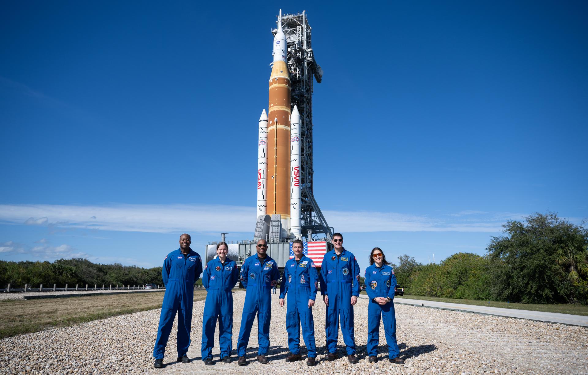 Artemis II backup crewmembers Andre Douglas and Jenni Gibbons, and prime crewmembers Victor Glover, Reid Wiseman, Jeremy Hansen, and Christina Koch, pose in front of NASA’s Space Launch System rocket and Orion spacecraft, secured to the mobile launcher.