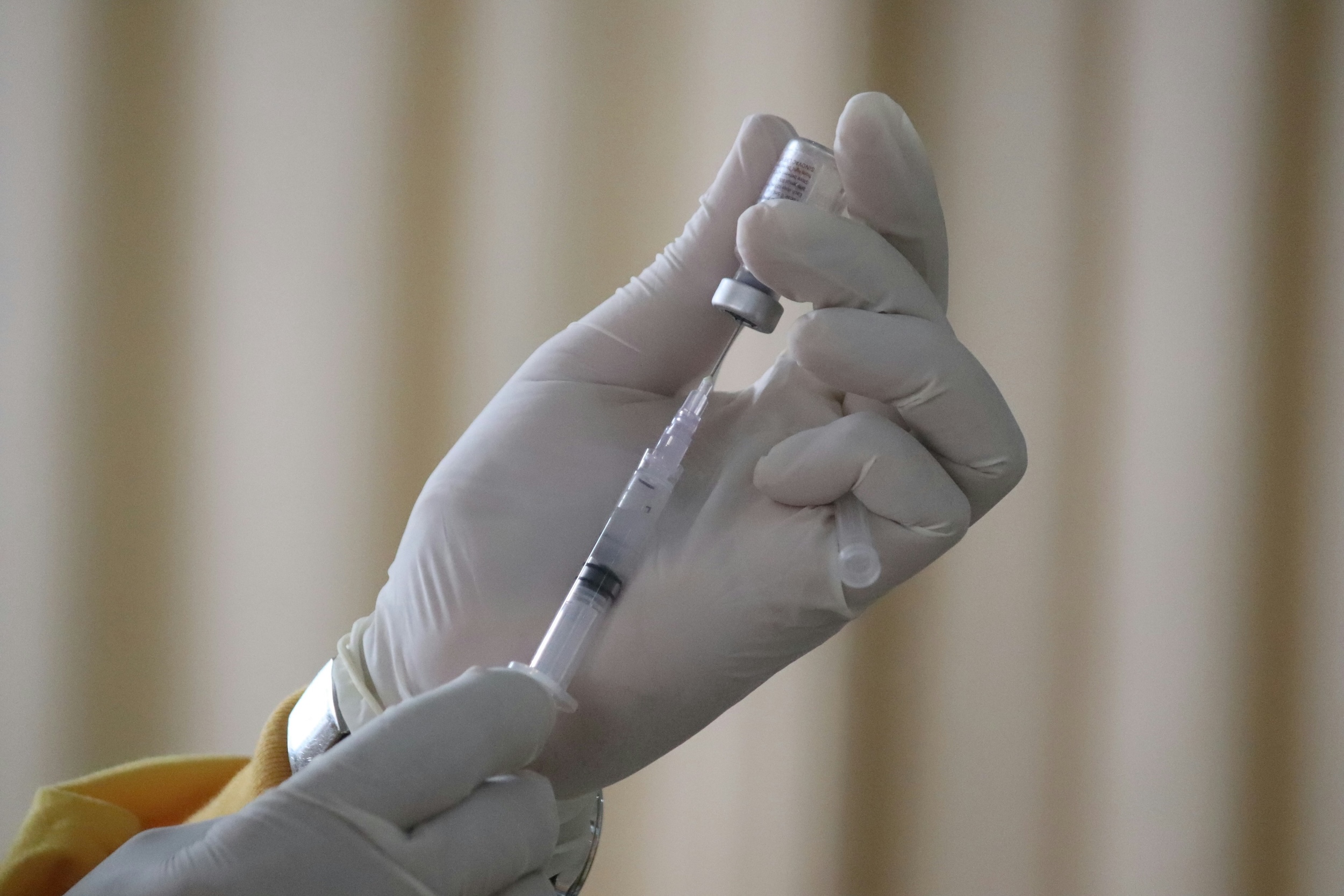 A pair of hands with medical gloves draws a vaccine out with a syringe.