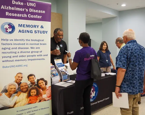 A group of people talks with representatives at a booth for the Duke-UNC Alzheimer's Disease Research Center.