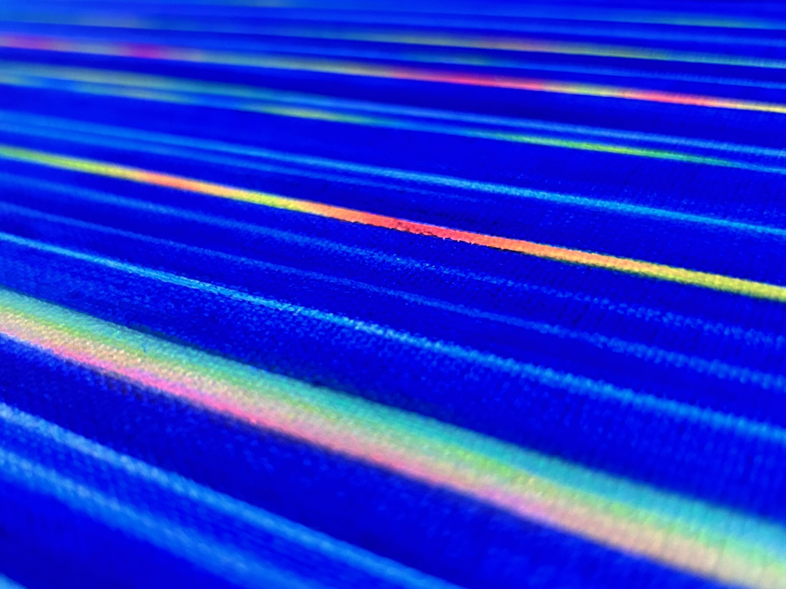 A close-up of a canvas with a royal blue base. Painted on top are lines in varying colors.