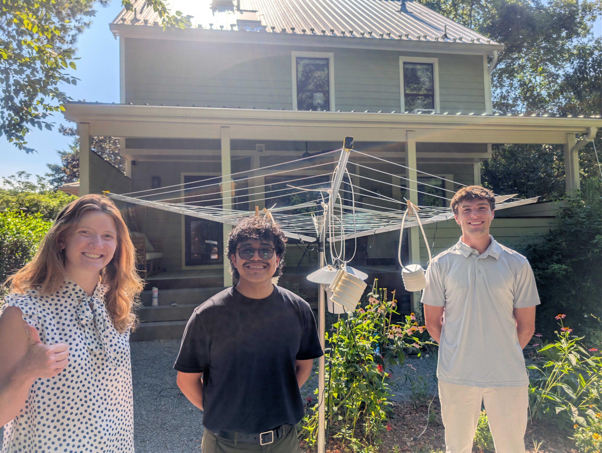 Three students smile in front of a contraption with monitoring instruments attached to it.