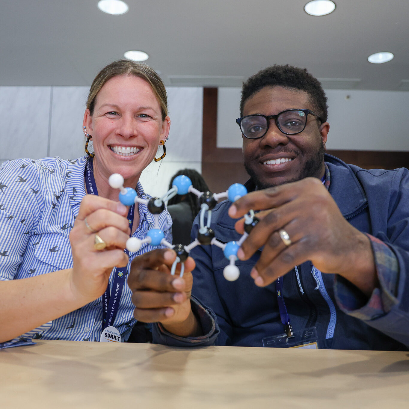 Two professionals smile while holding up a molecular model.