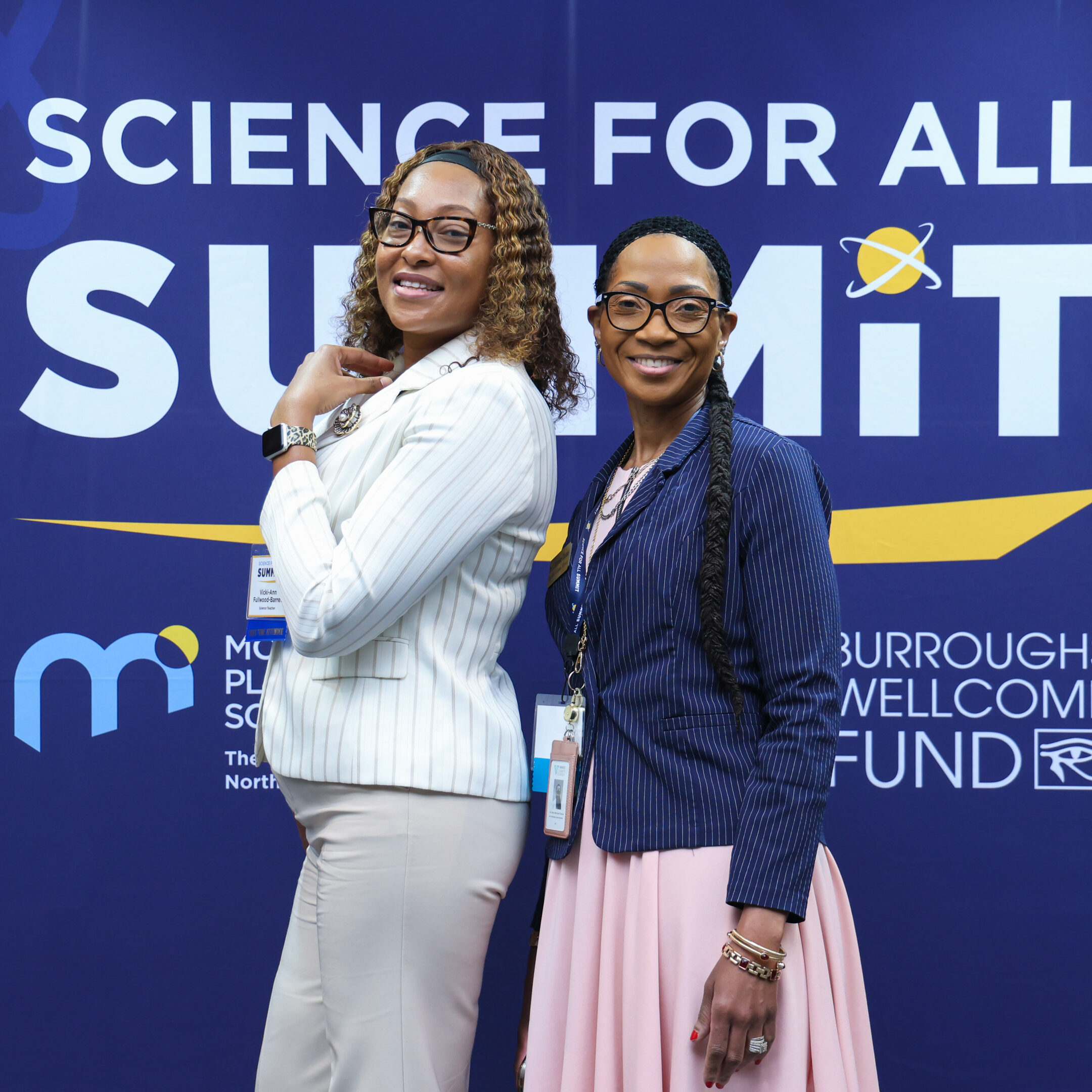 Two women pose in front of a Science for All Summit backdrop.